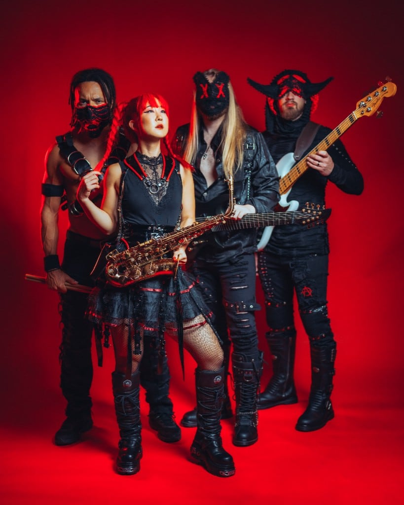 DEADGRACE against a red backdrop: Grace Kelly in front with a saxophone, flanked by the masked drummer, guitarist and bassist